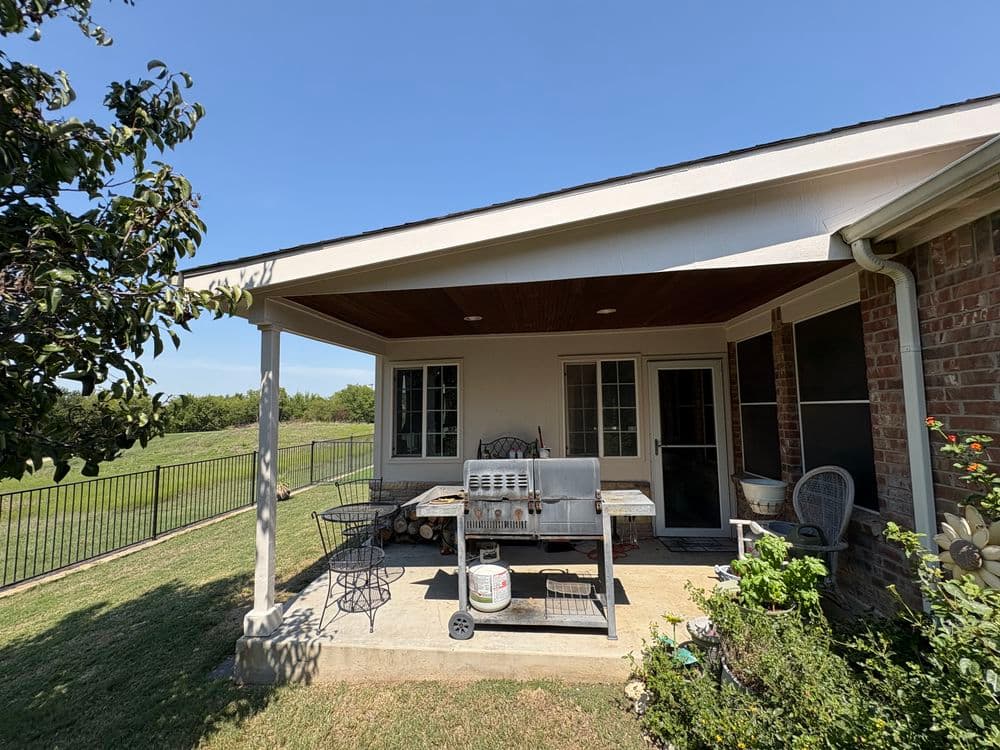 Patio with grill and seating area, green lawn in background, bright sunny day.