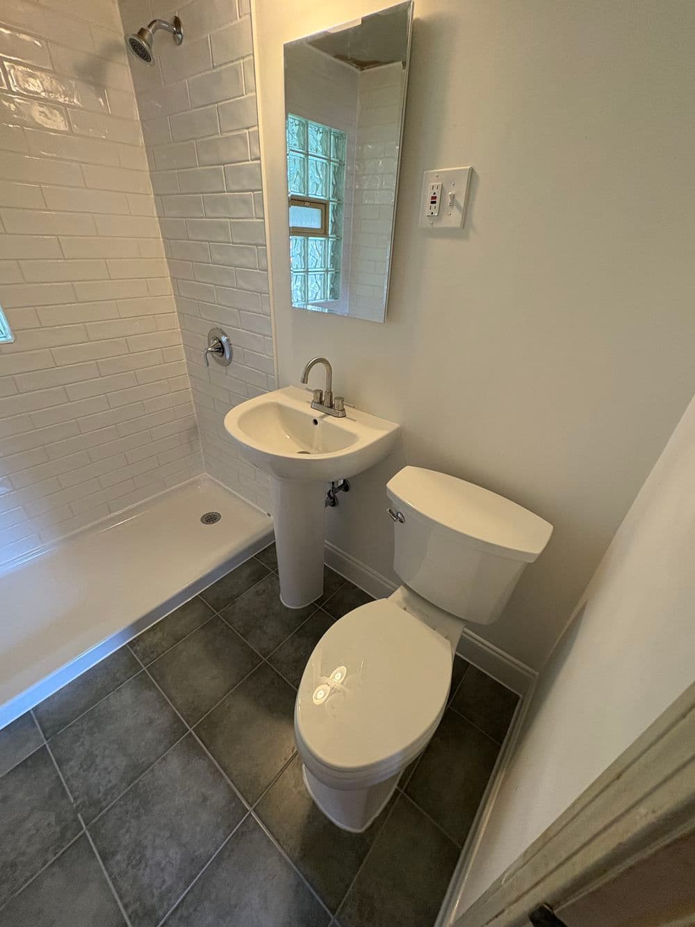 Modern bathroom with shower, pedestal sink, and toilet featuring tiled floor and bright lighting.