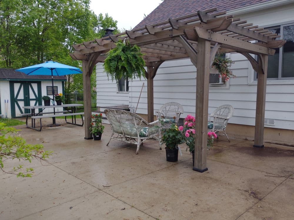 Pergola with seating area, potted flowers, and an umbrella in a patio setting.