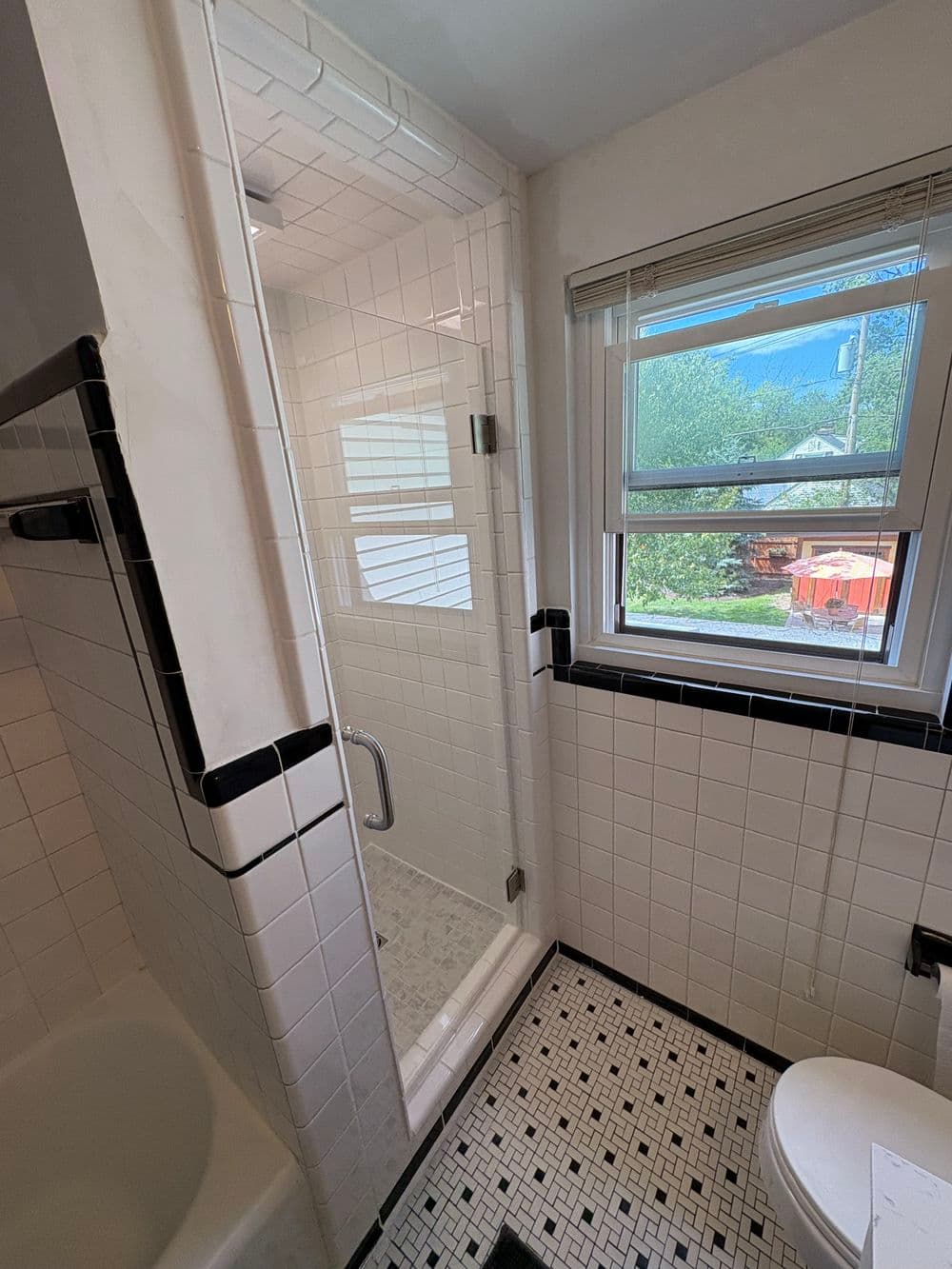 Modern bathroom featuring a tiled shower, large window, and classic black and white decor.