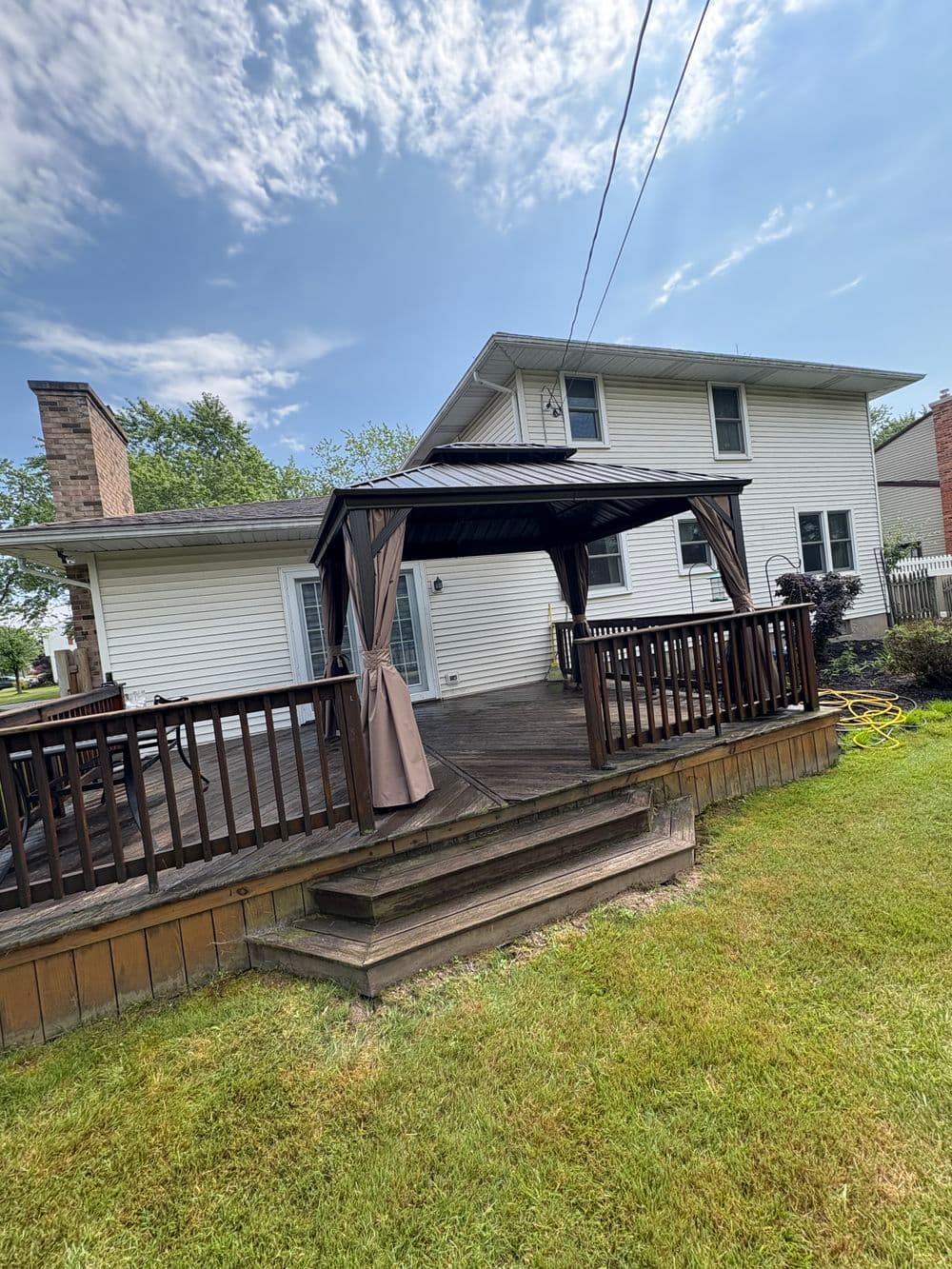 Wooden deck with gazebo and lawn, sunny day, residential home backdrop.