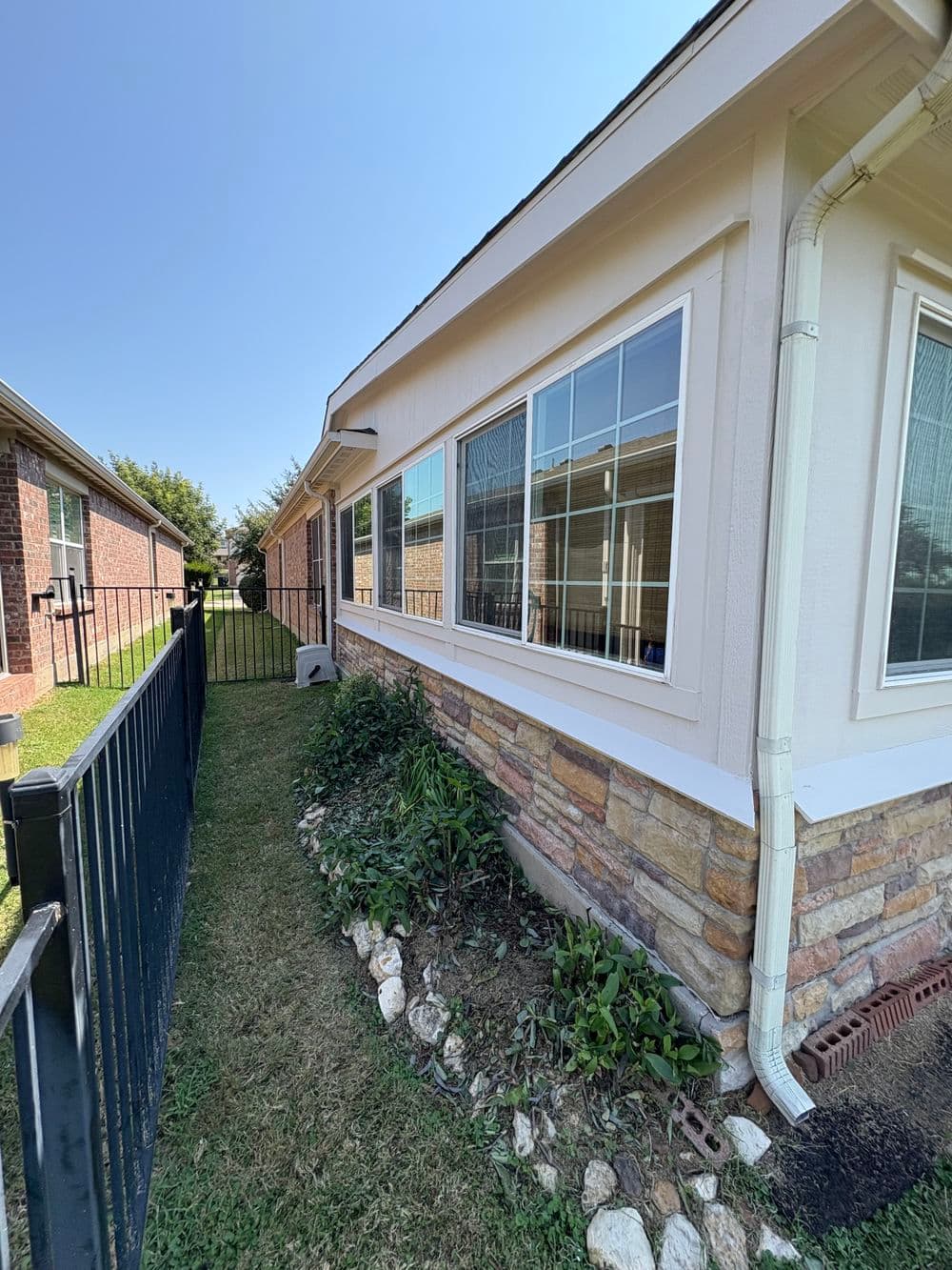 Side view of a house featuring stone siding, large windows, and a fenced yard.