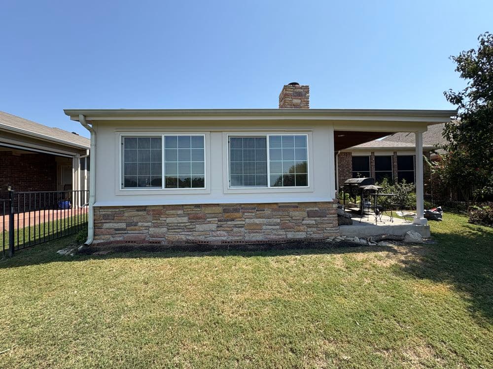 Cozy house exterior featuring a stone-clad sunroom and a well-maintained grassy yard.