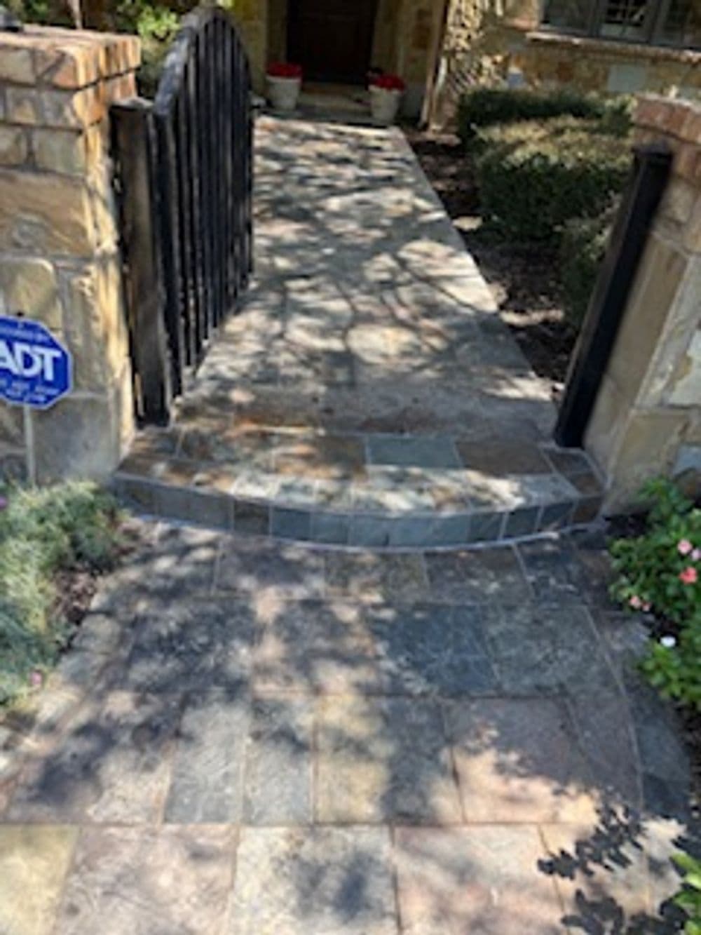 Stone pathway leading to a home entrance with a black wrought iron gate and greenery.
