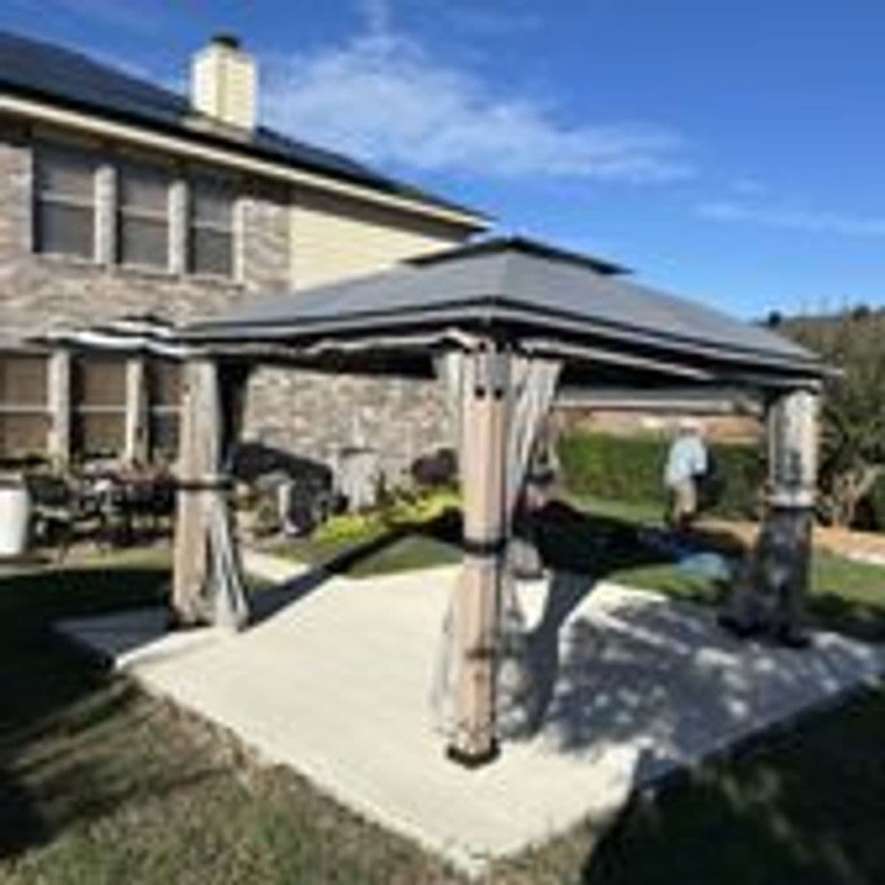 Backyard gazebo with curtains on a stone patio, sunny day, house in the background.