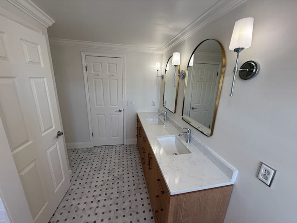 Modern bathroom with dual sinks, gold-framed mirrors, and patterned tile flooring.