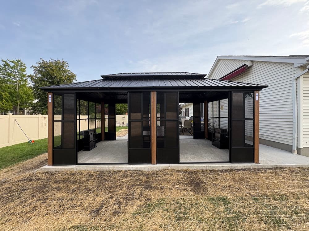 Modern screened-in gazebo with black mesh panels and a metal roof in a backyard setting.