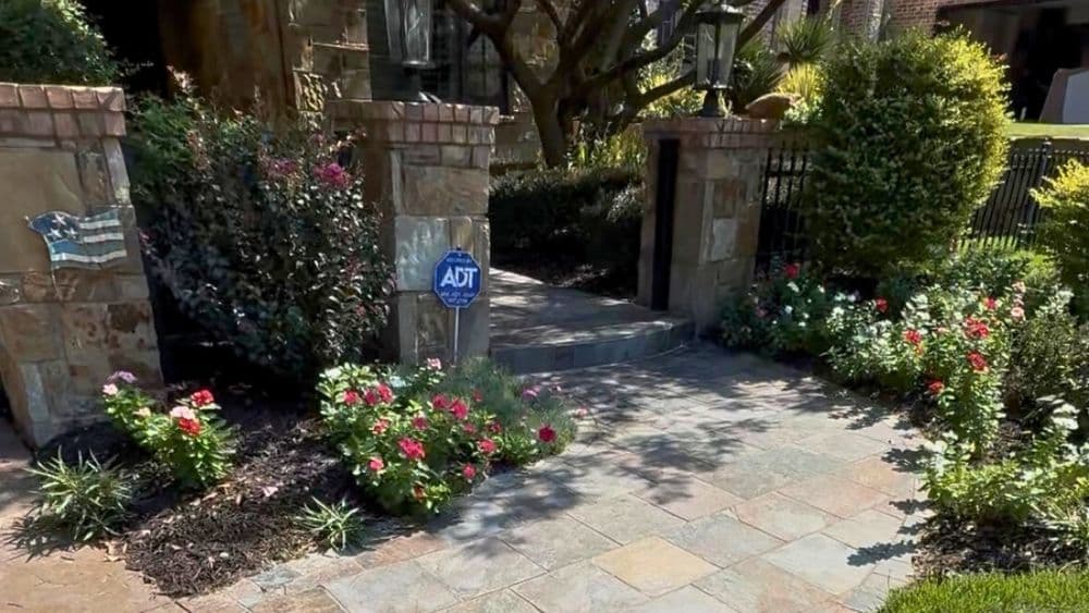 Beautiful landscaped entrance with flowers, stone walkway, and security sign.